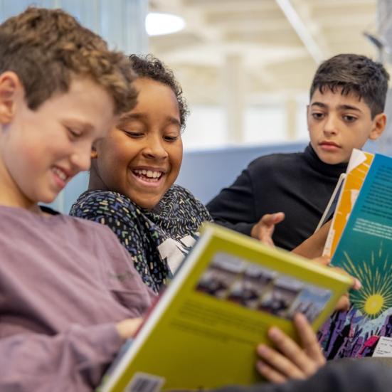 Tre smilende drenge læser i bøger på biblioteket