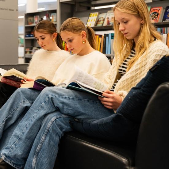 Tre unge piger læser i en sofa på et bibliotek